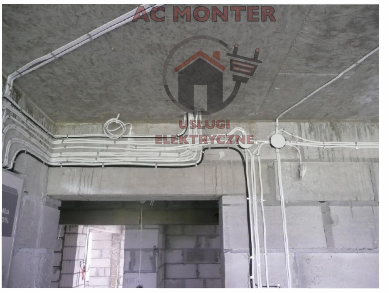 Białe kable elektryczne ułożone w peszlach na surowym betonowym suficie i ścianach w trakcie budowy, widoczne puszki instalacyjne i otwór drzwiowy w tle.