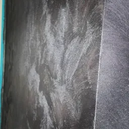 Ściana z dekoracyjną, ciemną powłoką z widocznymi śladami pędzla i delikatnym połyskiem, ujęcie z boku.