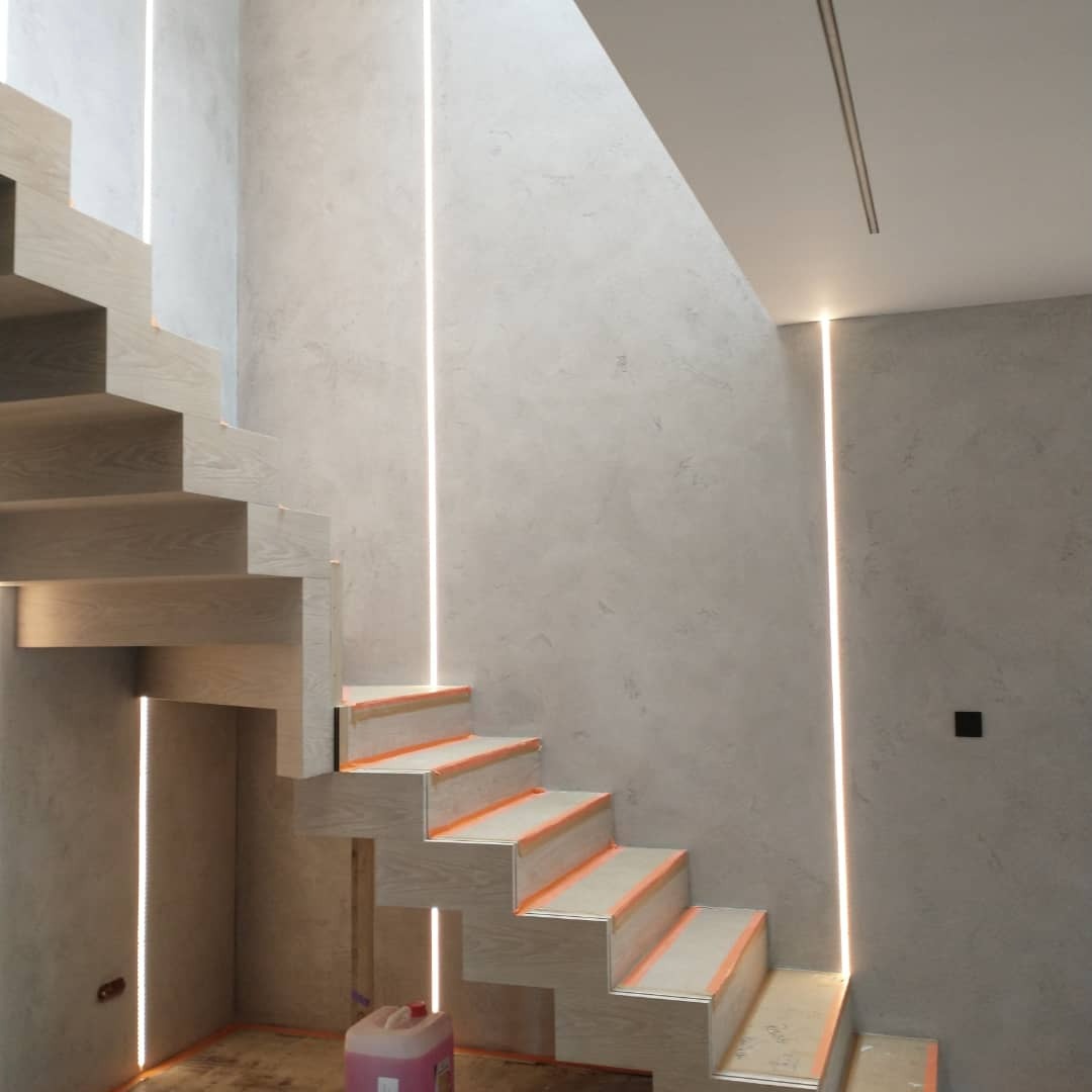 Nowoczesne schody drewniane z oświetleniem LED wpuszczonym w ścianę, zabezpieczone taśmą malarską przed zabrudzeniem, ściany wykończone w stylu betonu architektonicznego.
