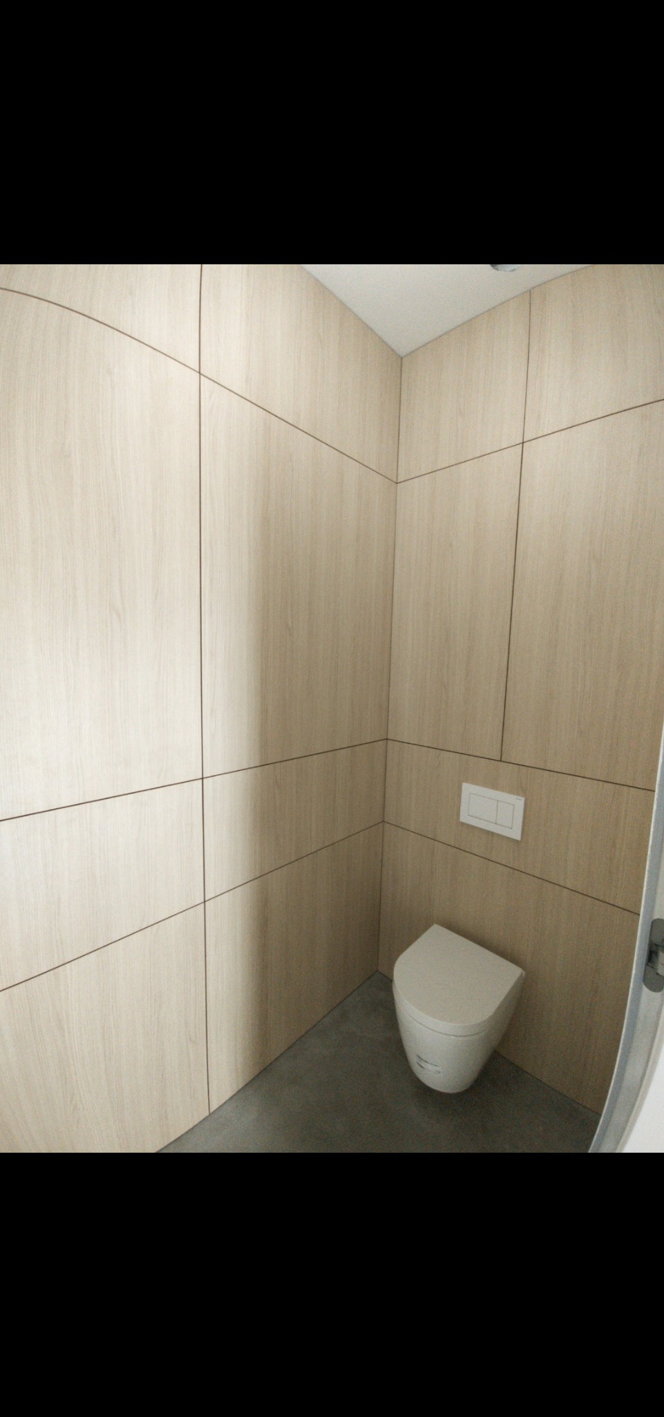 Wykończona toaleta z drewnopodobnymi panelami ściennymi ułożonymi w kwadraty i wiszącą miską WC na szarej podłodze.