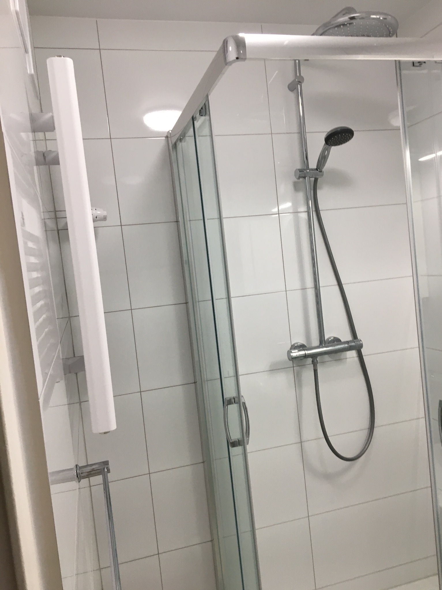 Nowoczesna kabina prysznicowa z deszczownicą i panelem prysznicowym na tle białych, kwadratowych płytek