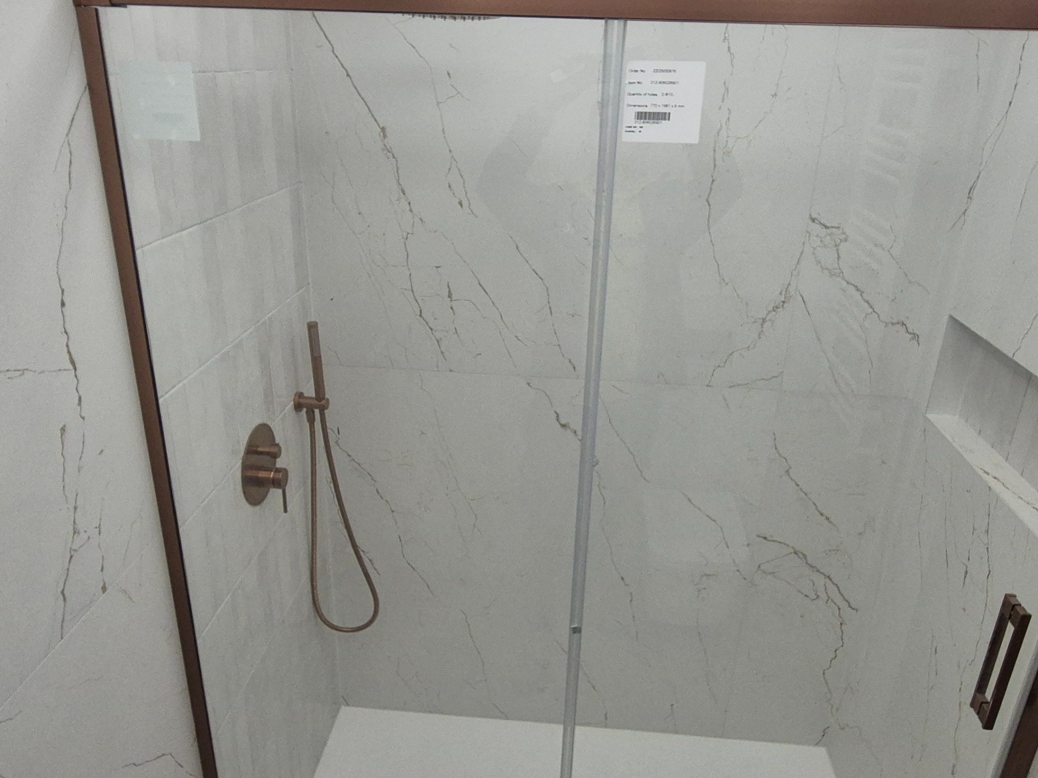 Wykończona kabina prysznicowa z brązowymi detalami i marmurowymi płytkami. Widoczna bateria i wnęka w ścianie. Nowoczesny design łazienki.