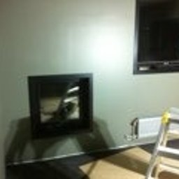 Panorenno - Wnęka w ścianie przygotowana pod montaż kominka, widoczna instalacja elektryczna, drabina oparta o ścianę, surowy stan wykończenia.