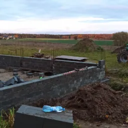 Fundamenty domu jednorodzinnego w trakcie budowy w Gdyni, z widocznymi bloczkami betonowymi, wystającymi prętami zbrojeniowymi i butelką wody na wierzchu.