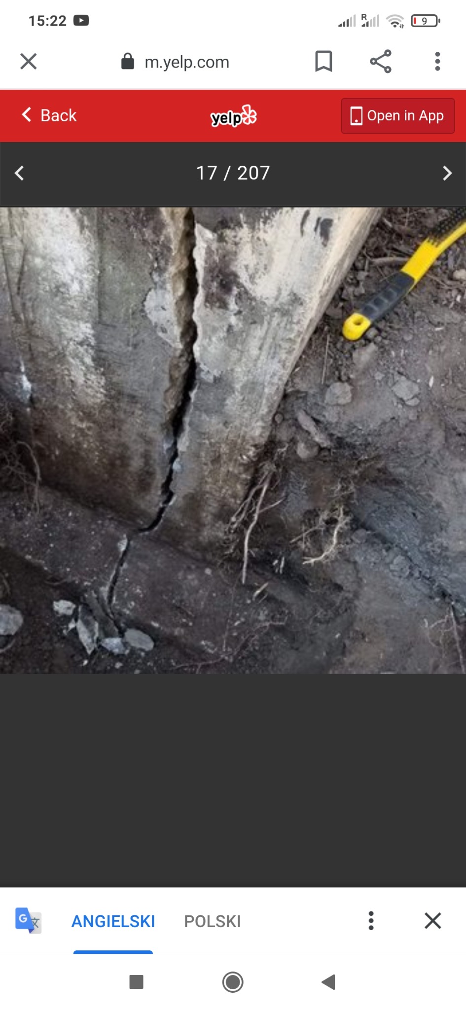 Pęknięty betonowy element konstrukcyjny z widocznymi śladami wilgoci i żółtą rączką narzędzia w tle.