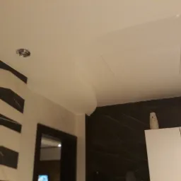 Biały sufit z ukrytym włazem rewizyjnym i oświetleniem punktowym, dekoracyjna ściana w geometryczne wzory i marmurowe wykończenie.