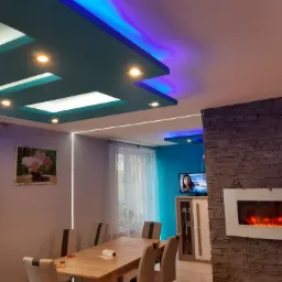 Salon z podwieszanym sufitem z oświetleniem LED, lampami punktowymi i dekoracyjnym kominkiem elektrycznym na ścianie z kamienia.