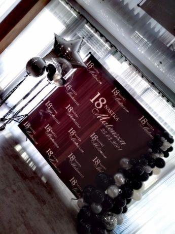 Dekoracja na 18 urodziny: bordowa ścianka z napisem '18 Nastka Mateusza 25.03.2004' otoczona czarno-białymi balonami i balonami w kształcie gwiazd.