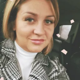 Portret uśmiechniętej kobiety w płaszczu w pepitkę i białym golfie, siedzącej w samochodzie, z filtrem dodającym różowe konfetti.