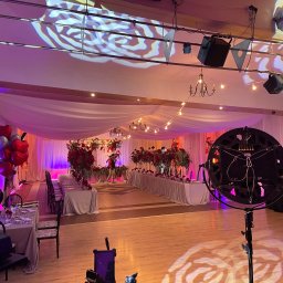 DJ Wodzirej Prezenter muzyczny MiOdzieniec Maciej Jaśkowiak - Sala bankietowa z oświetleniem scenicznym: reflektory, dekoracje kwiatowe, balony w kształcie serc, przygotowana do imprezy. Romantyczny nastrój.