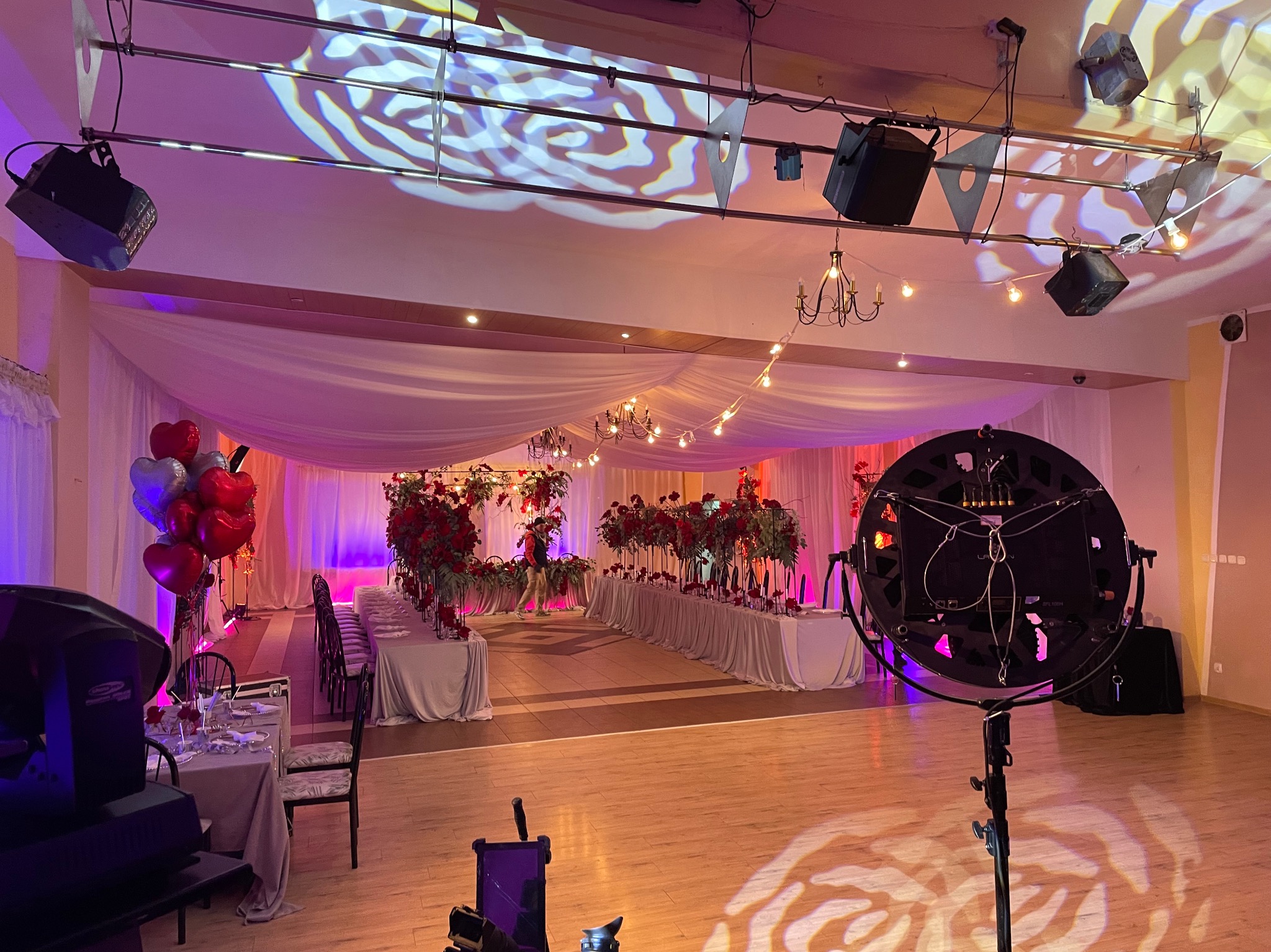 Sala bankietowa z oświetleniem scenicznym: reflektory, dekoracje kwiatowe, balony w kształcie serc, przygotowana do imprezy. Romantyczny nastrój.