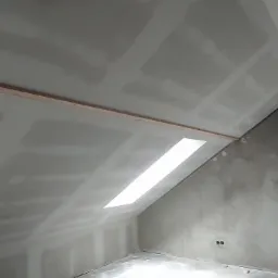 Poddasze w trakcie prac wykończeniowych: ściany i skośny sufit pokryte płytami gipsowo-kartonowymi, widoczne łączenia płyt i drewniana listwa mocująca, przygotowane do dalszych prac.