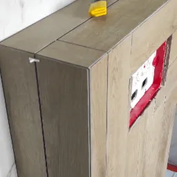 Obudowa stelaża WC wykończona płytkami imitującymi drewno, z widocznymi krzyżykami dystansowymi i nożykiem do cięcia płytek na górze, na tle marmurowej ściany.