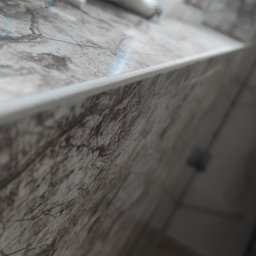 Firma Usługowa Martyna Kowal - Fragment blatu z marmurowym wzorem, obok okna, z widocznymi akcesoriami: śrubokrętem, szmatką i butelką płynu czyszczącego.