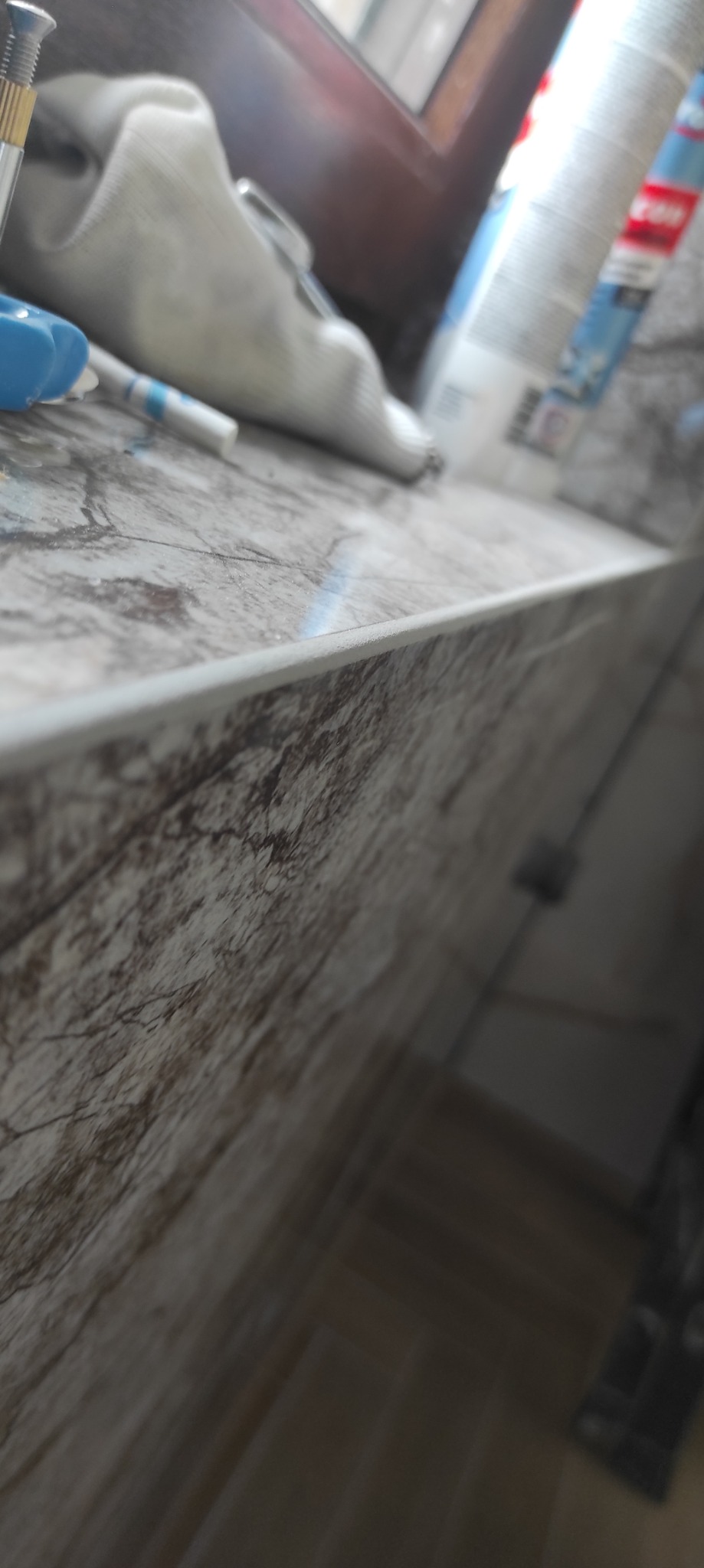 Fragment blatu z marmurowym wzorem, obok okna, z widocznymi akcesoriami: śrubokrętem, szmatką i butelką płynu czyszczącego.