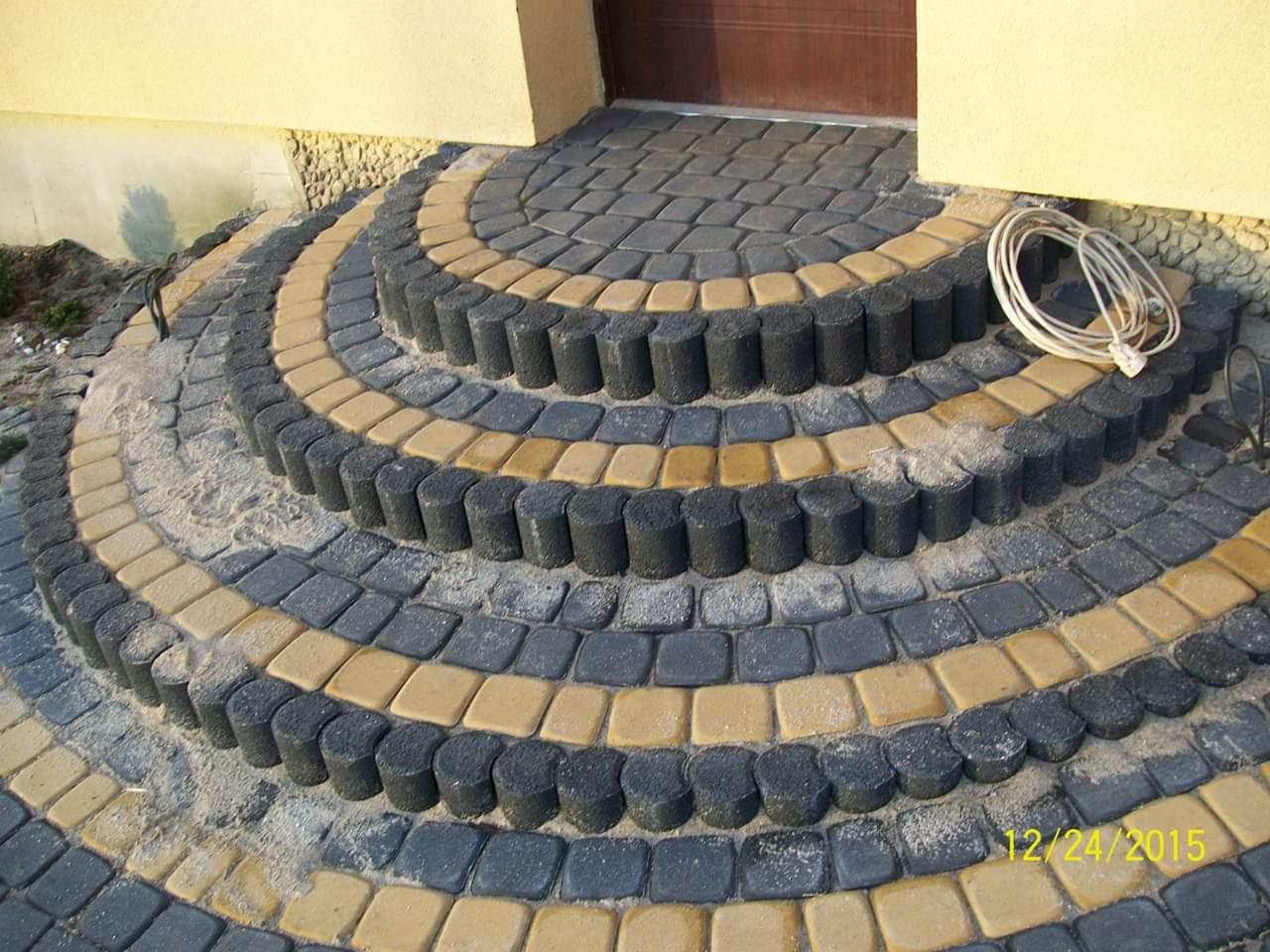 Półokrągłe schody wejściowe ułożone z kostki brukowej w kolorach szarym i piaskowym, z widocznym przewodem elektrycznym obok.