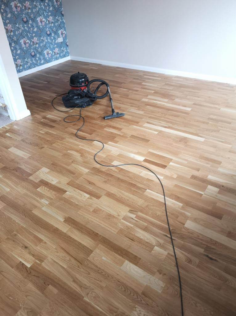 Świeżo położony, jasny parkiet w pokoju z niebieską tapetą w kwiaty; odkurzacz przemysłowy na podłodze, przygotowany do sprzątania po pracach.