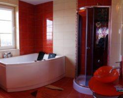 Czerwono-biała łazienka z narożną wanną, kabiną prysznicową i umywalką na postumencie. Na wannie leżą czarne ręczniki.