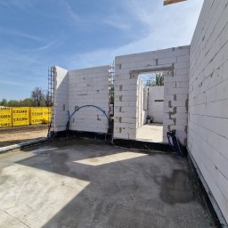 FINISZ USŁUGI REMONTOWO BUDOWLANE SPÓŁKA Z OGRANICZONĄ ODPOWIEDZIALNOŚCIĄ SPÓŁKA Z OGRANICZONĄ ODPOWIEDZIALNOŚCIĄ - Wnętrze budowanego domu z bloczków Ytong, widoczne ściany w trakcie wznoszenia, betonowa posadzka i przygotowane materiały budowlane na zewnątrz.