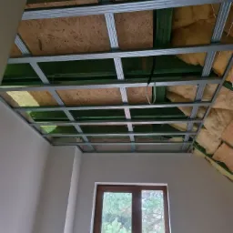 Stelaż sufitowy z profili metalowych, płyty OSB i izolacji z wełny mineralnej w nowym domu, widok od dołu, okno na tle drzew