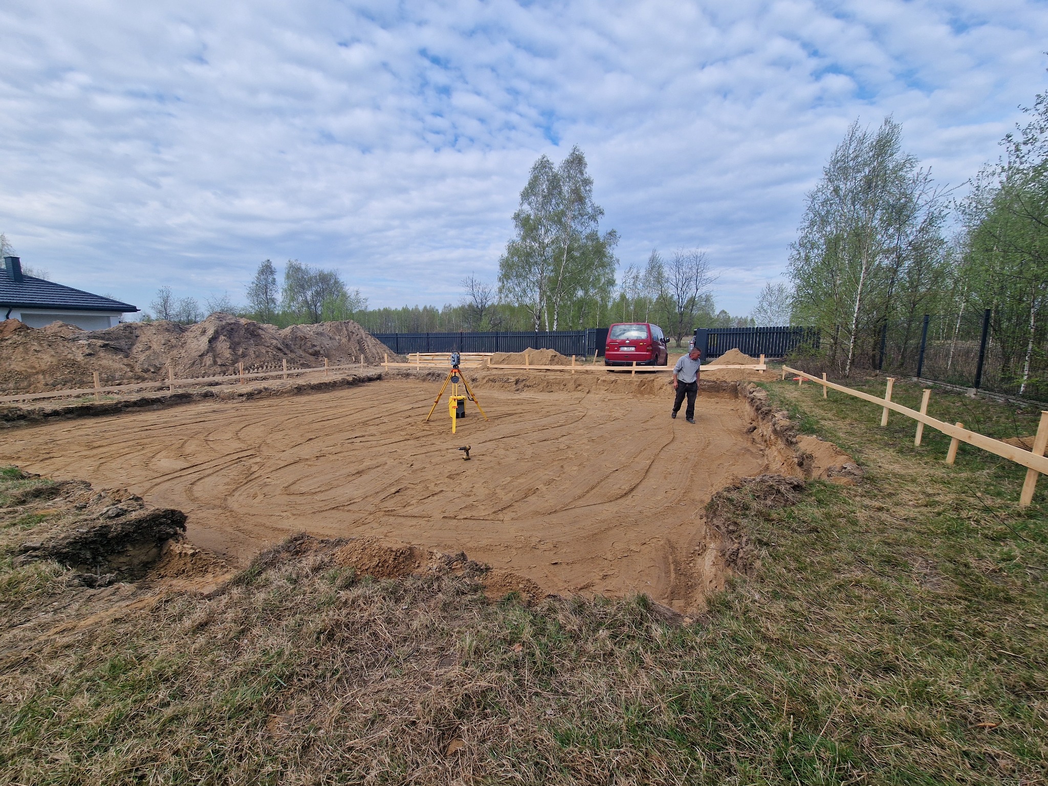 Wytyczony teren pod budowę domu jednorodzinnego z widocznym niwelatorem i drewnianymi stemplami szalunkowymi.