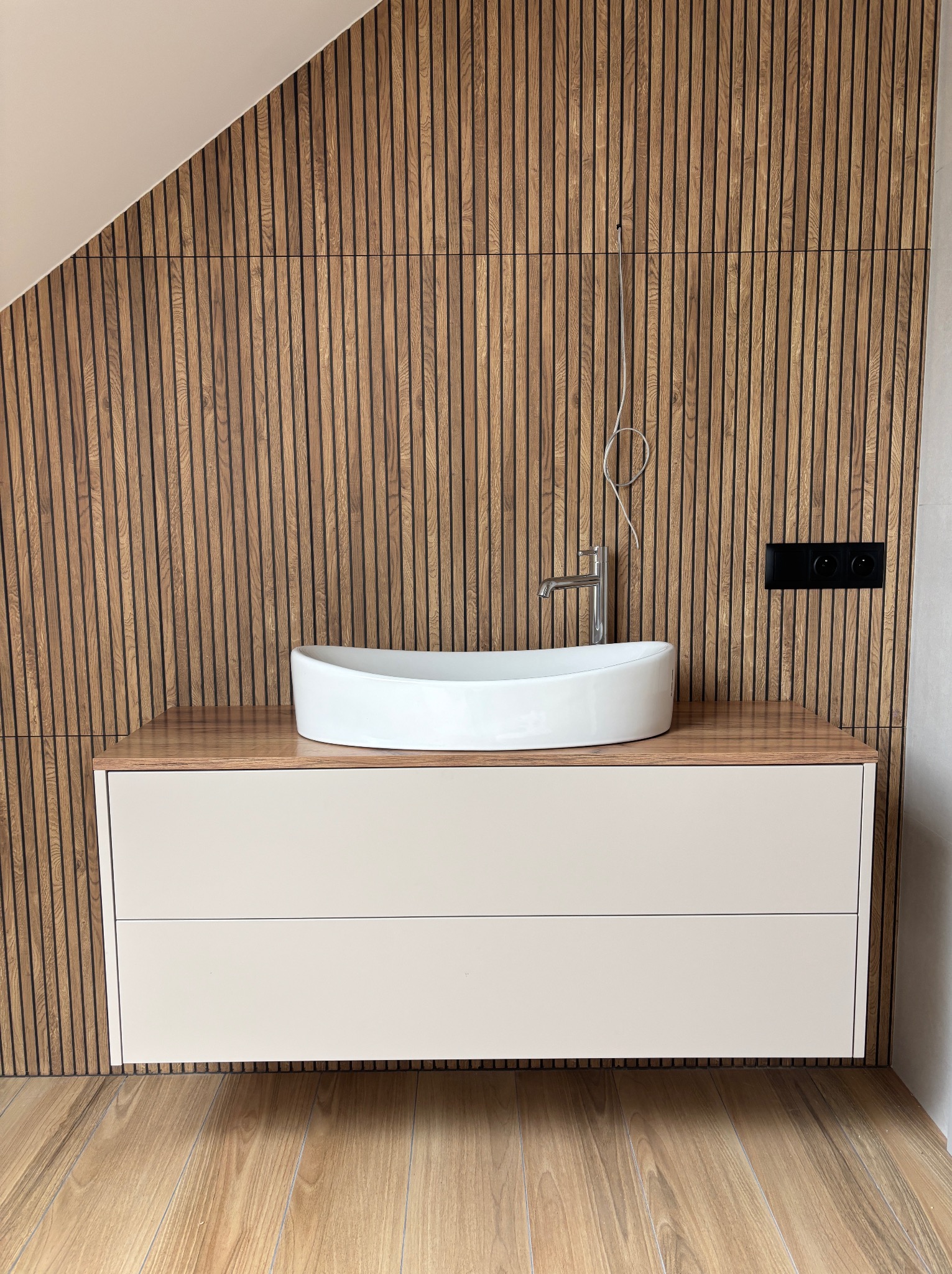 Nowoczesna łazienka z umywalką nablatową i szafką z szufladami, drewniane lamele na ścianie i podłodze w odcieniach brązu, minimalistyczny design.