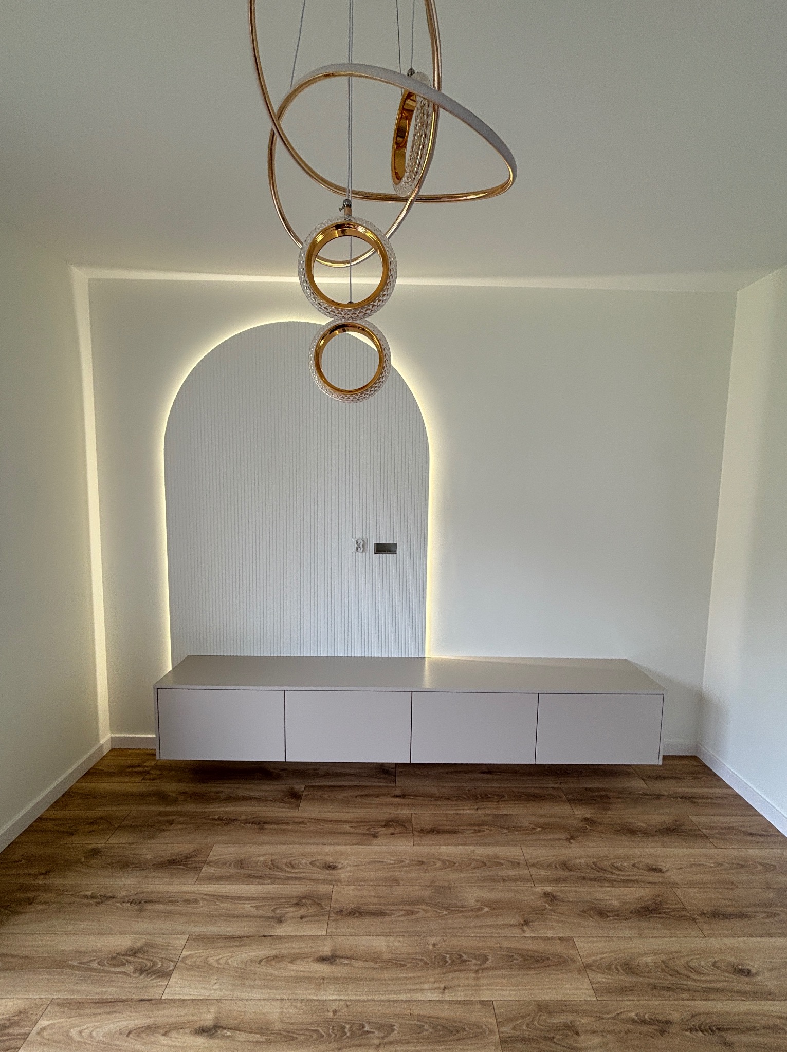 Nowoczesna szafka RTV w salonie z podświetlaną wnęką i designerską lampą. Minimalistyczny design, drewniana podłoga, jasne ściany.