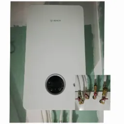 Biały, wiszący piec gazowy Bosch z cyfrowym wyświetlaczem, podłączony do instalacji z zaworami odcinającymi; montaż w trakcie wykańczania ścian gipsowo-kartonowych.