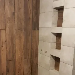 Wykończona ściana łazienki z płytek imitujących drewno oraz wnęki wyłożone szarymi płytkami.