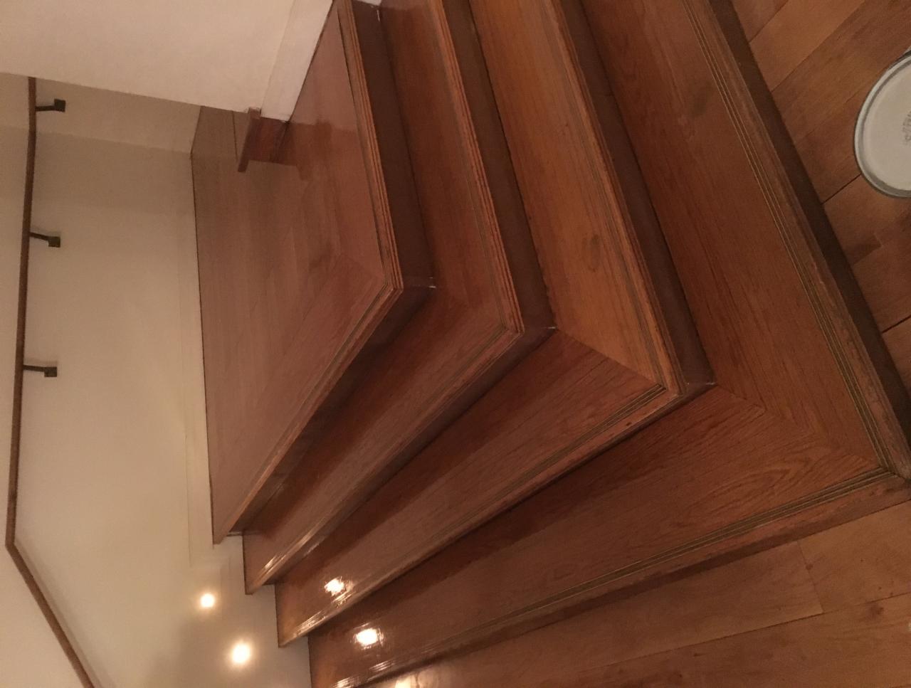 Polerowane drewniane schody z widocznymi śladami świeżego lakieru, ujęcie z góry, widoczna podłoga z parkietu i ściana w tle.