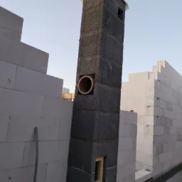 Wznoszenie komina z pustaków szamotowych na budowie domu z białych bloczków, widoczny fragment wentylacji