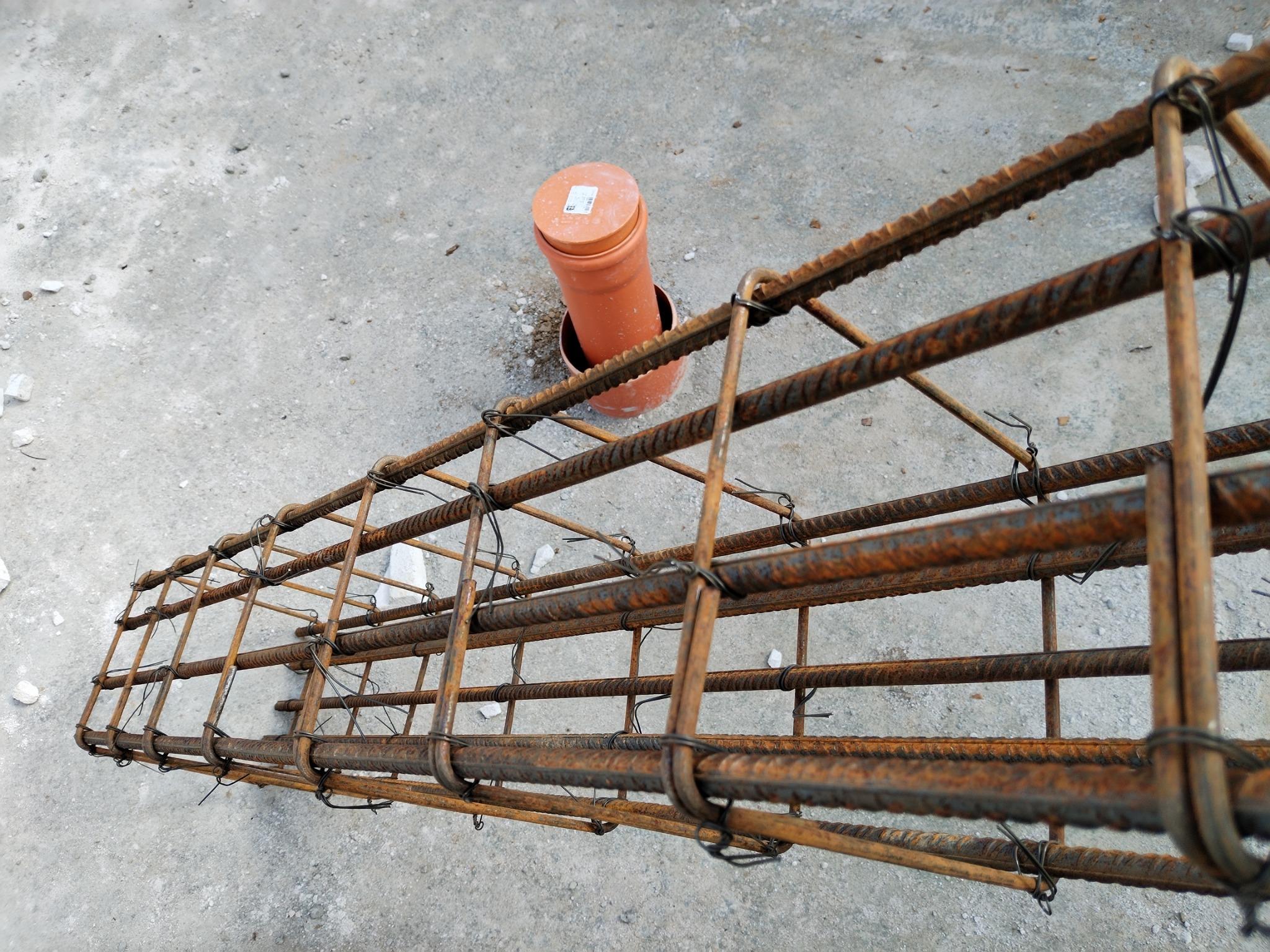 Zbrojenie fundamentowe z rurą kanalizacyjną wystającą z ziemi, widoczne ślady rdzy na prętach.