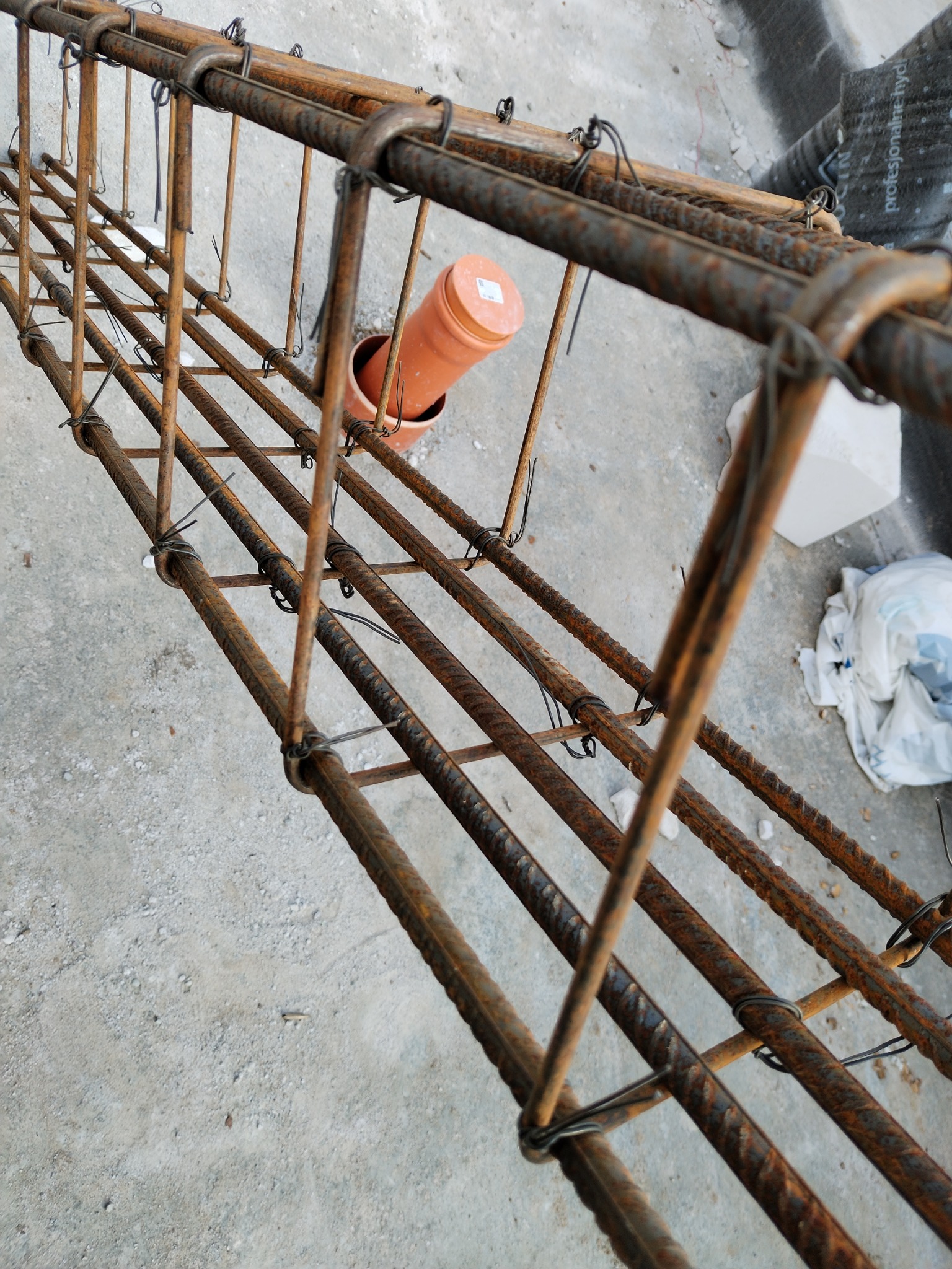 Zbrojenie fundamentowe z rurą kanalizacyjną wewnątrz, widoczne druty wiązałkowe i betonowe podłoże.