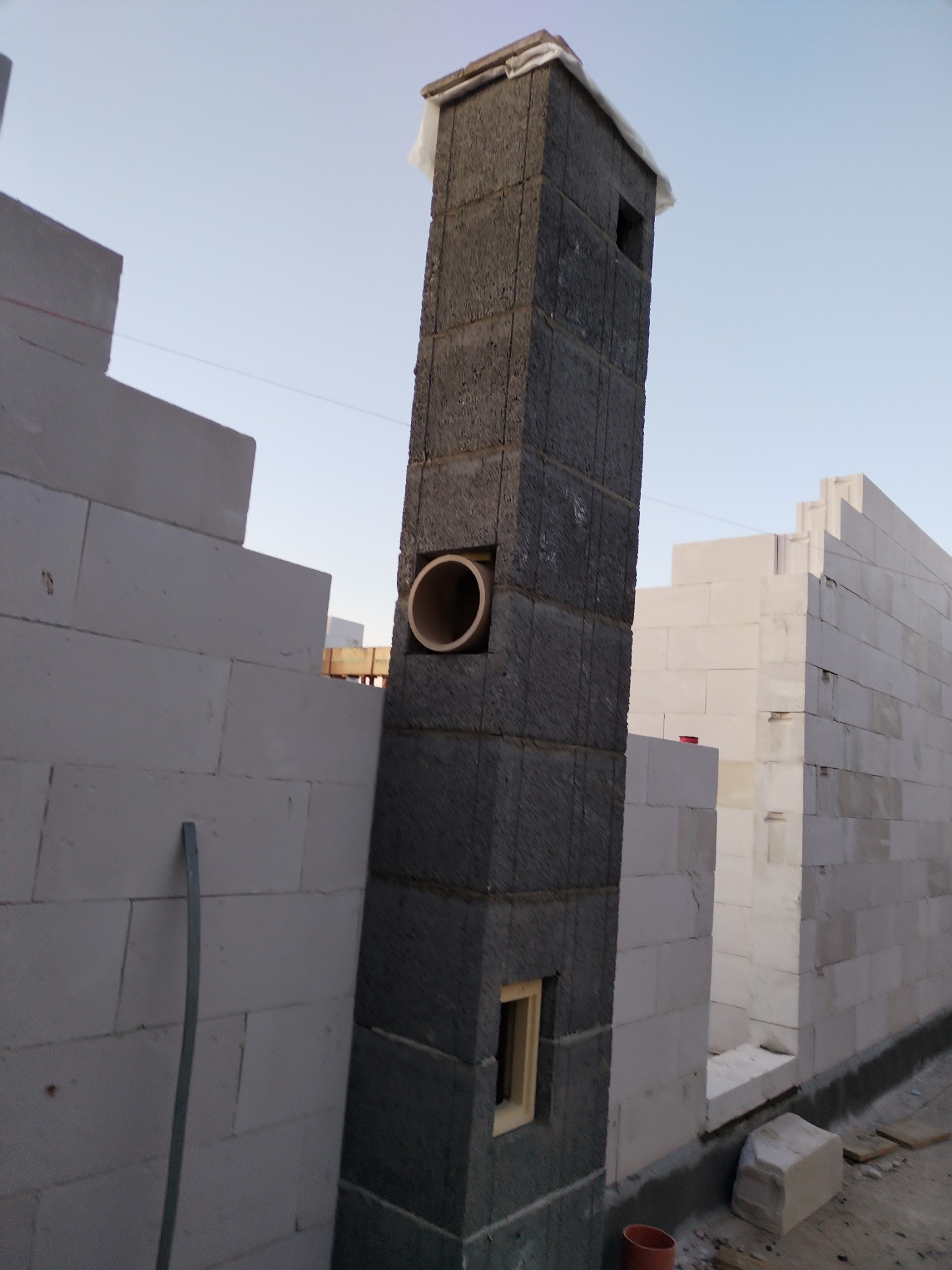 Wznoszenie komina z pustaków szamotowych na budowie domu z białych bloczków, widoczny fragment wentylacji