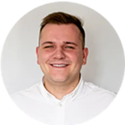 Uśmiechnięty młody mężczyzna w białej koszuli na jasnym, neutralnym tle.