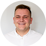 Uśmiechnięty młody mężczyzna w białej koszuli na jasnym, neutralnym tle.