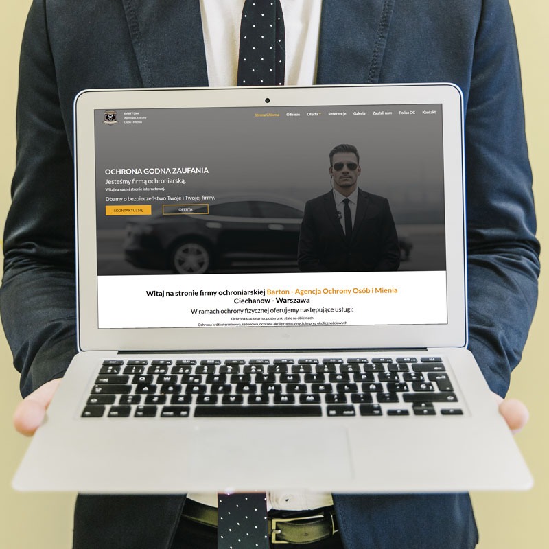 Osoba w garniturze trzyma laptopa, na ekranie strona internetowa firmy ochroniarskiej Barton, z hasłem 'Ochrona godna zaufania' i zdjęciem ochroniarza.