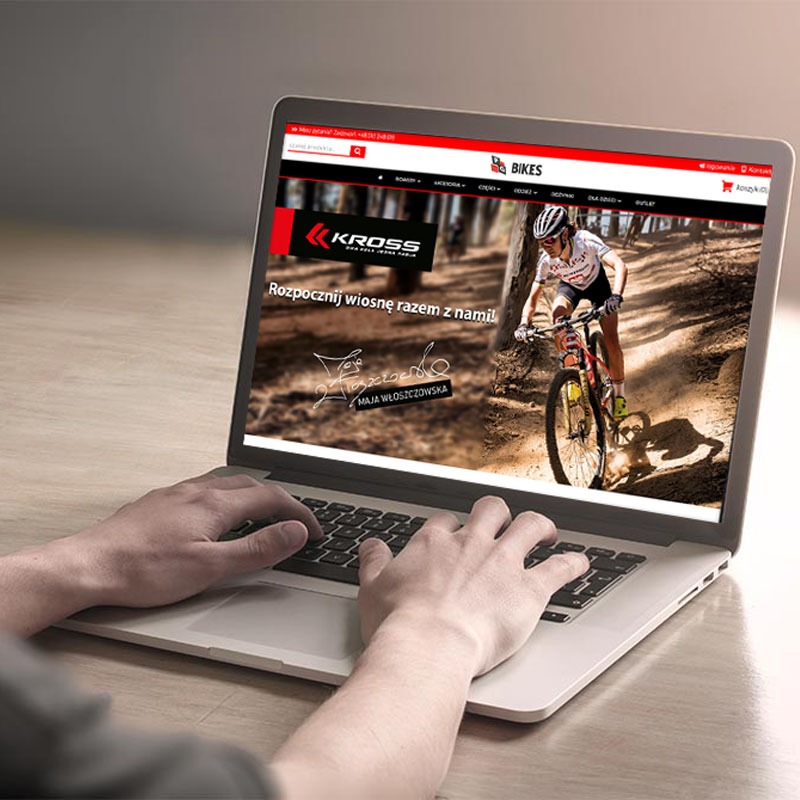 Osoba przegląda na laptopie stronę rowerowego sklepu internetowego z logo Kross i zdjęciem Mai Włoszczowskiej na rowerze górskim.