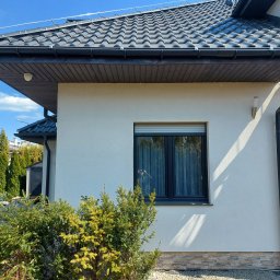 ELEKTRO- INSTAL ANDRZEJ KOWALIK - Zewnętrzny widok domu z zainstalowanym systemem odgromowym, widoczne elementy zabezpieczające na dachu i przewodzie odprowadzającym wzdłuż ściany, na tle błękitnego nieba.