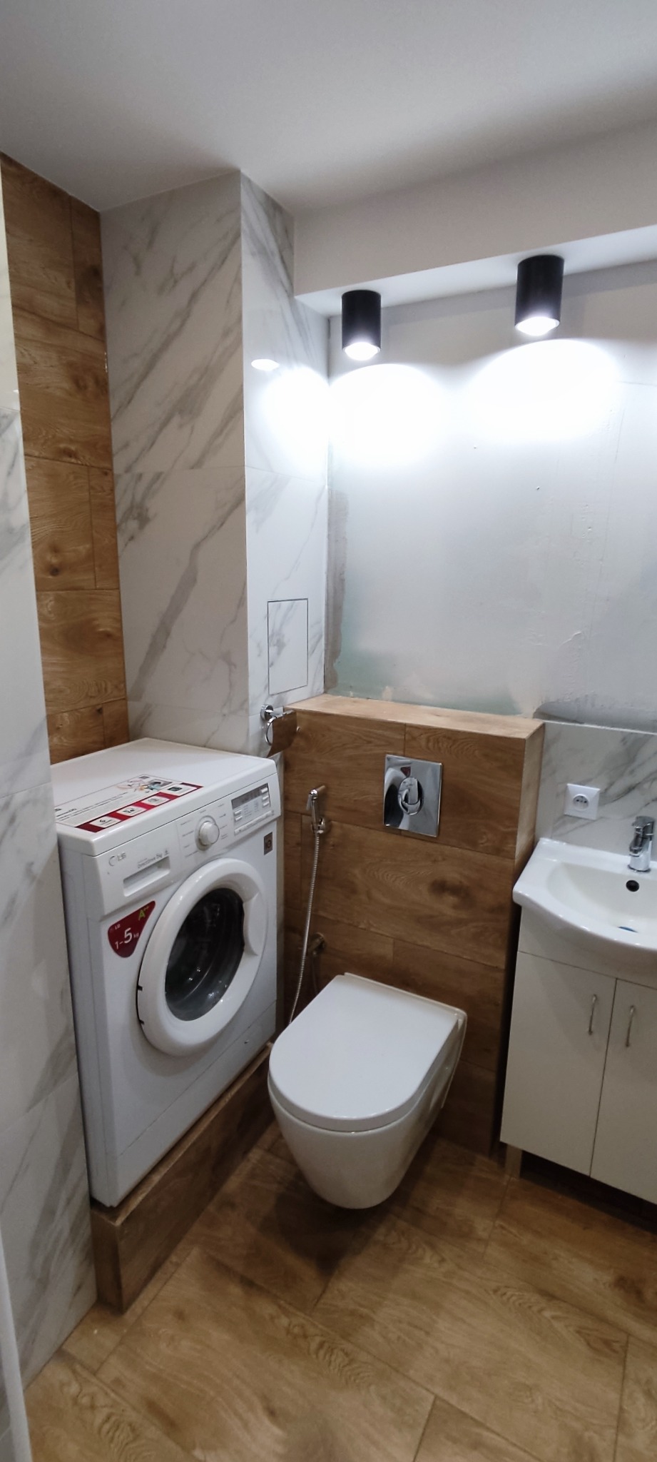 Nowoczesna aranżacja łazienki w Klementowicach z pralką, wiszącą toaletą z bidetką i umywalką w szafce, wykończona płytkami imitującymi marmur i drewno.