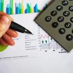 Dłoń z długopisem nad wykresem finansowym, obok kalkulator. Analiza danych i planowanie budżetu.