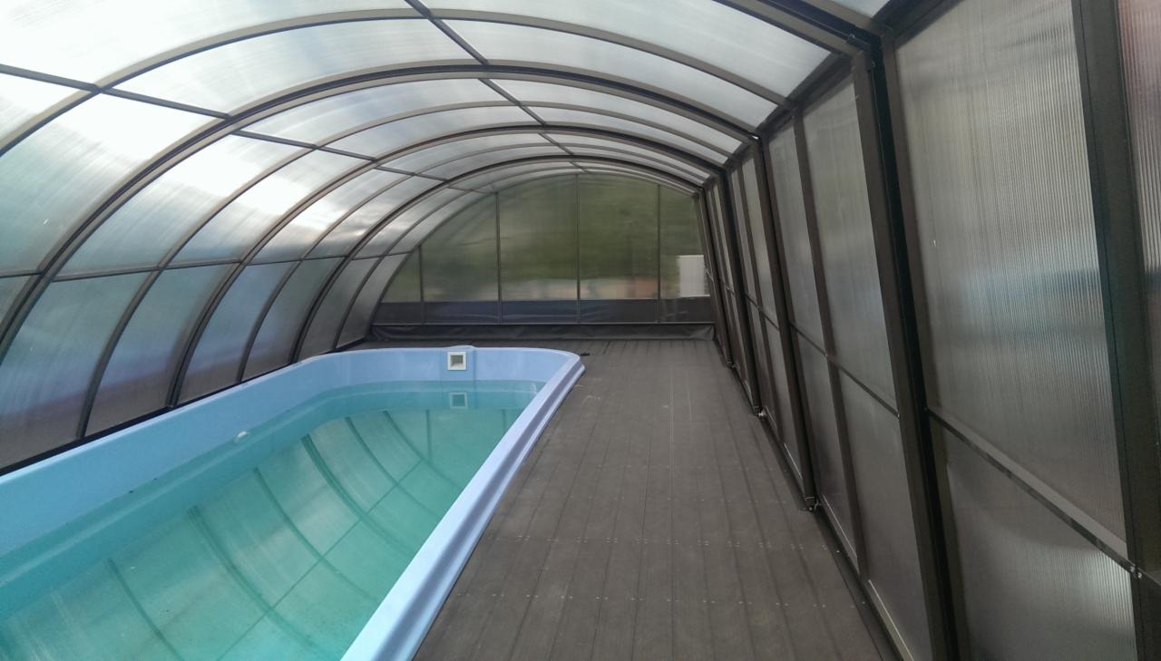 Zadaszony basen z poliwęglanu z drewnianym podestem, widok z wnętrza konstrukcji.