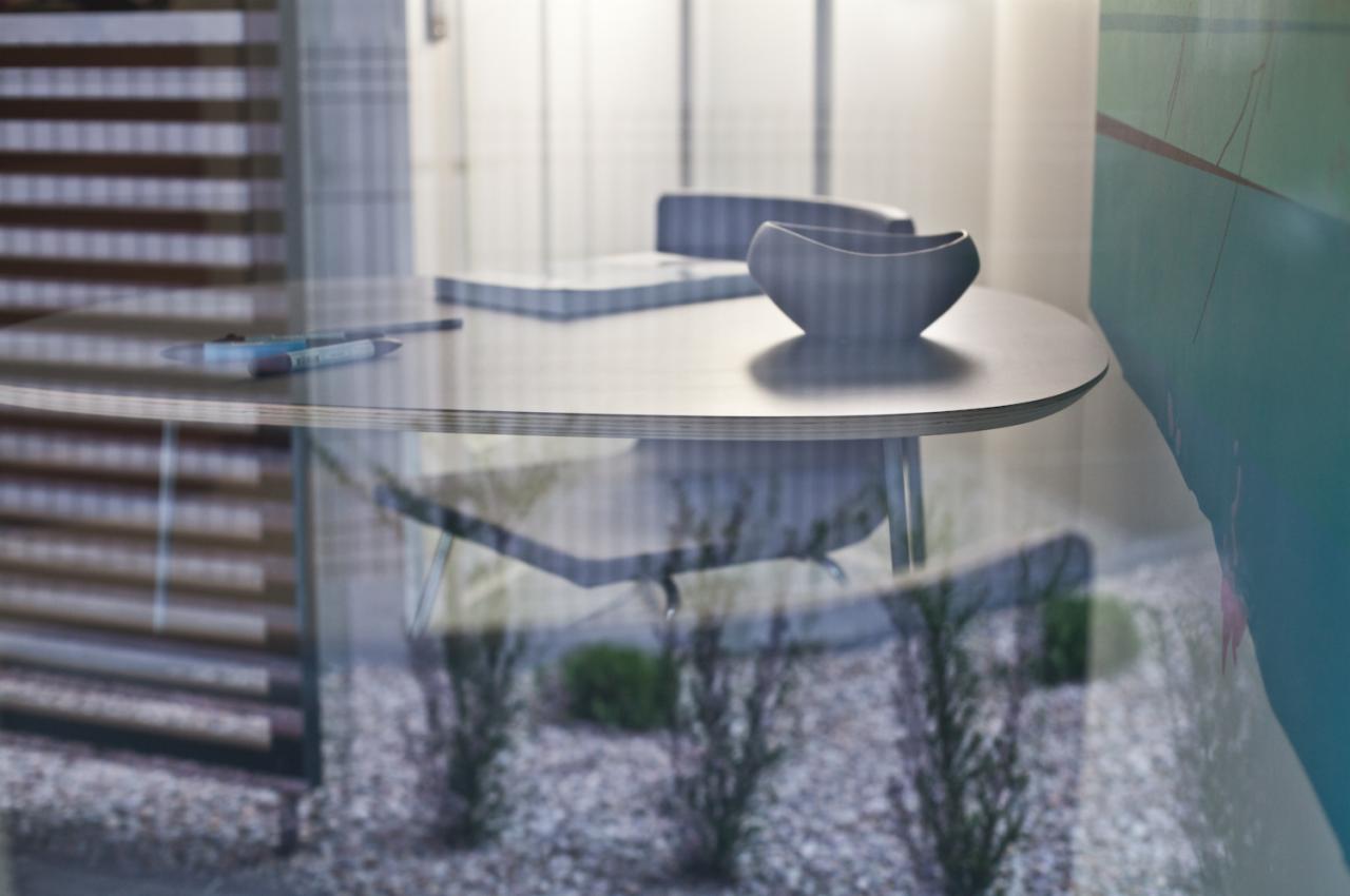 Okrągły stolik z miseczką i notatnikiem w gabinecie, widoczne odbicia roślin w szklanej powierzchni.