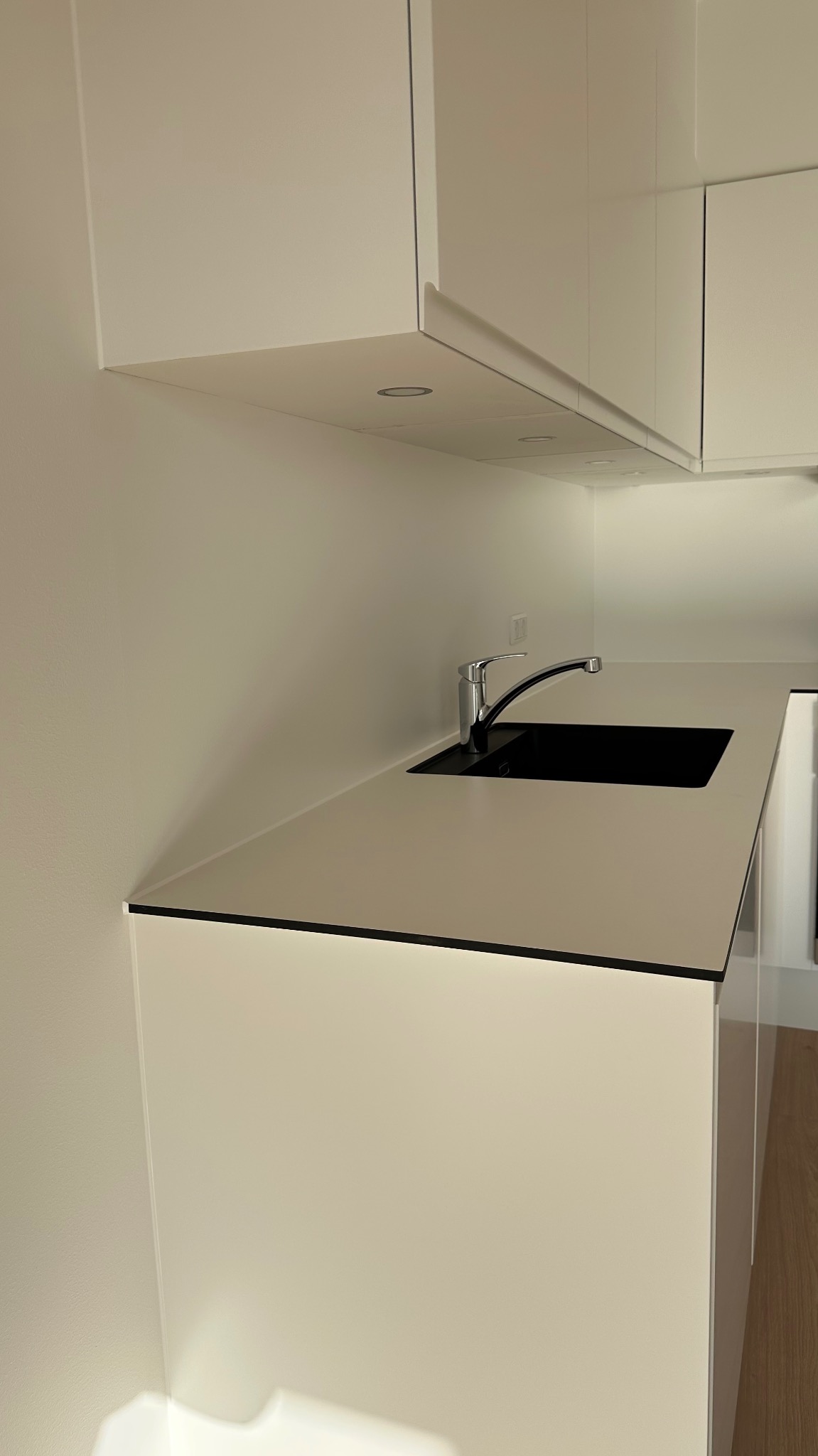 Nowoczesna, minimalistyczna kuchnia z białymi szafkami, czarnym zlewem i chromowaną baterią, oświetlenie podszafkowe LED, gładkie ściany.