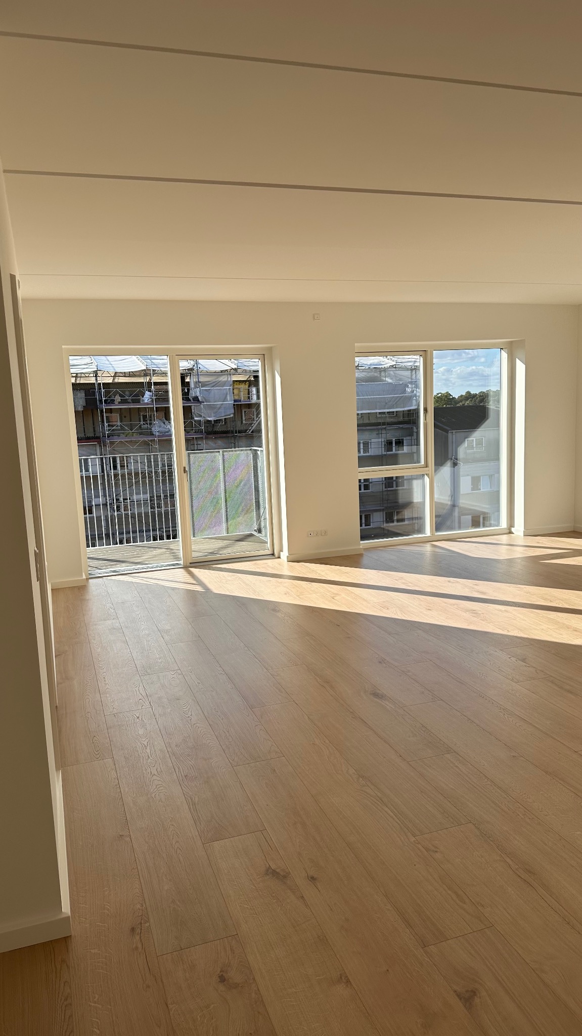 Jasne panele podłogowe w nowym, pustym mieszkaniu z widokiem na budynek w rusztowaniach przez balkon i okno.