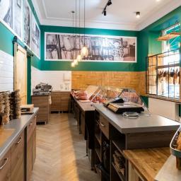 IG Design - Wnętrze sklepu z zielonymi ścianami, drewnianymi elementami i ekspozycją pieczywa oraz wędlin w chłodniach.