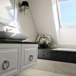 IG Design - Elegancka łazienka na poddaszu z białą armaturą, umywalką nablatową, szafką z frezowanymi frontami i okrągłymi uchwytami, mozaiką przy wannie i storczykiem.