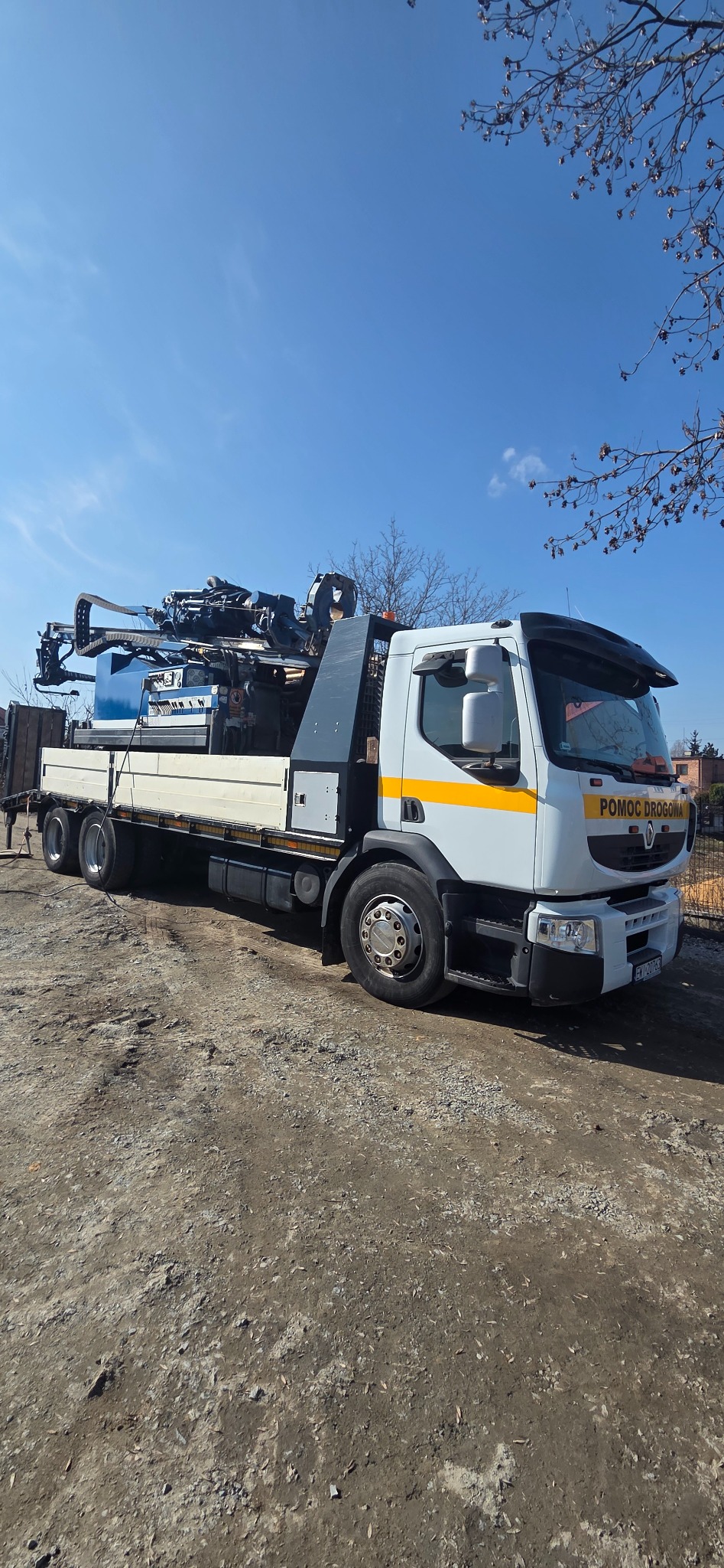 Ciężarówka pomocy drogowej z zamontowaną wiertnicą do studni głębinowych na platformie, zaparkowana na żwirowym podłożu w słoneczny dzień.