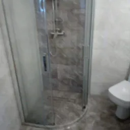 Szara łazienka z kabiną prysznicową z przezroczystego szkła i odpływem liniowym w podłodze z marmuru, widoczna również toaleta.