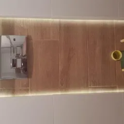 Świeżo wykafelkowana wnęka w łazience z podświetleniem LED, widoczny stelaż podtynkowy WC z chromowanym przyciskiem spłukującym oraz instalacja kanalizacyjna.